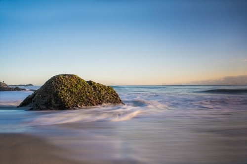 Moss covered stone in the swallow water of the ocean - Australian Stock Image