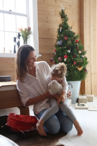 Mother and daughter cuddling with Christmas tree in background - Australian Stock Image