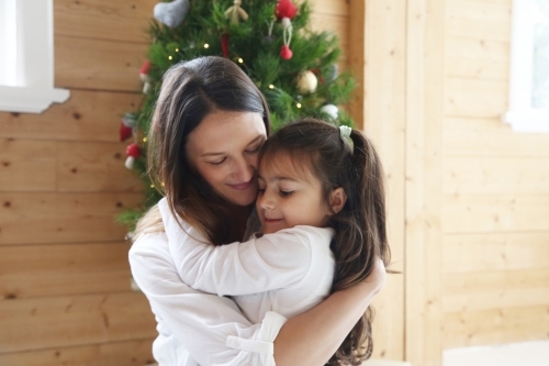 Mother and daughter hugging with Christmas tree in background - Australian Stock Image