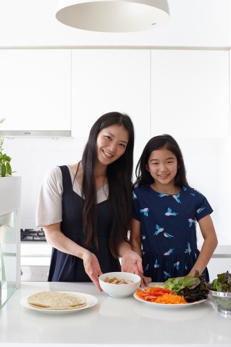 Mother and daughter in kitchen together preparing lunch - Australian Stock Image