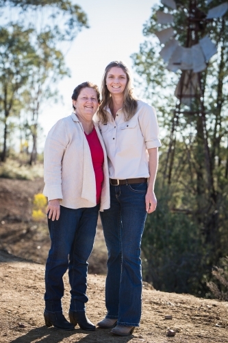 Mother and daughter on farm in drought with windmill smiling - Australian Stock Image