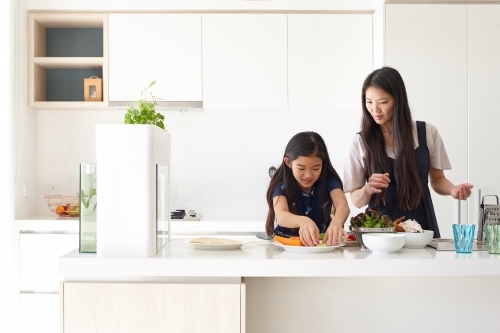 Mother and daughter preparing a meal together in kitchen - Australian Stock Image