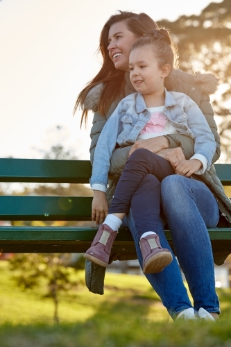 Mother and daughter sharing time laughing at park bench - Australian Stock Image