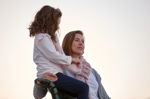 Mother and daughter sitting on park bench at park on sunset - Australian Stock Image