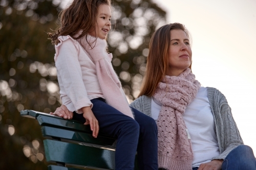 Mother and daughter sitting on park bench at park on sunset