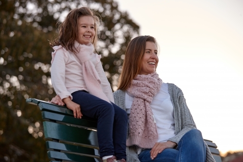 Mother and daughter sitting on park bench at park on sunset - Australian Stock Image