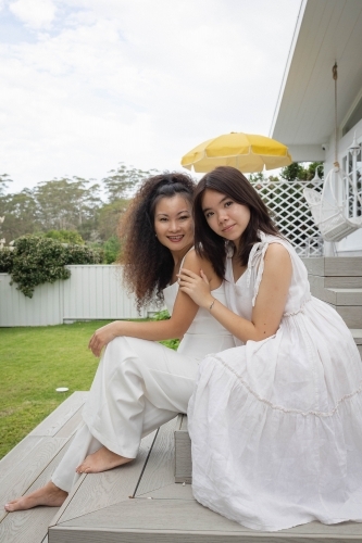 Mother and daughter sitting together on backyard steps - Australian Stock Image