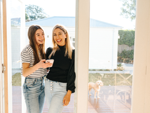 Mother and daughter standing in the doorway smiling. - Australian Stock Image