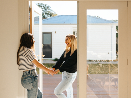 Mother and daughter standing in the doorway smiling while looking at each other and holding hands. - Australian Stock Image