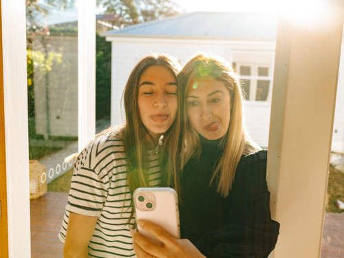 Mother and daughter taking selfies in the doorway. - Australian Stock Image