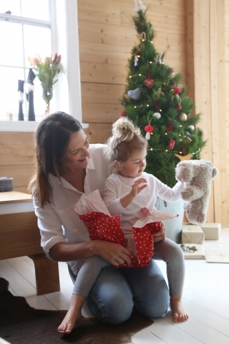 Mother and daughter unwrapping present with Christmas tree in background - Australian Stock Image