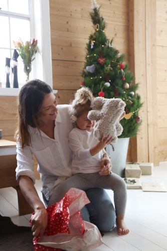 Mother and daughter unwrapping present with Christmas tree in background - Australian Stock Image