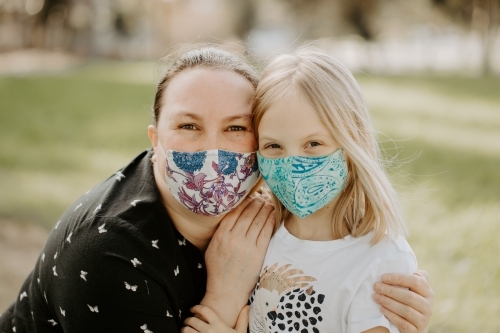 Mother and daughter wearing fabric masks during the corona virus COVID-19 pandemic hugging outside - Australian Stock Image