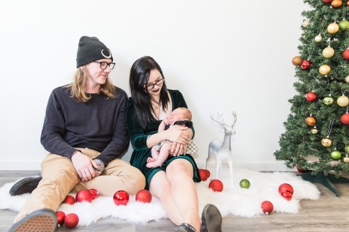 Mother and father smiling at baby in arms at Christmas with tree and decorations
