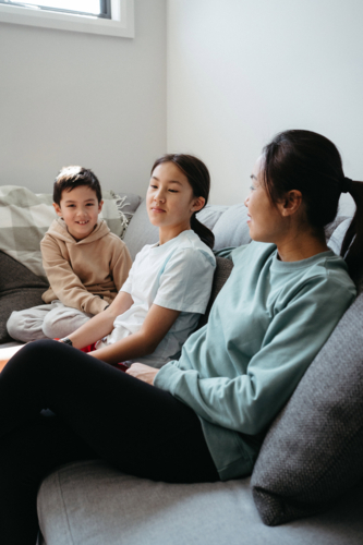 Mother and her kids gathered and seated in the entertainment room - Australian Stock Image