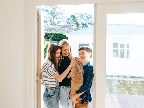 Mother and her kids holding a small dog in the doorway. - Australian Stock Image