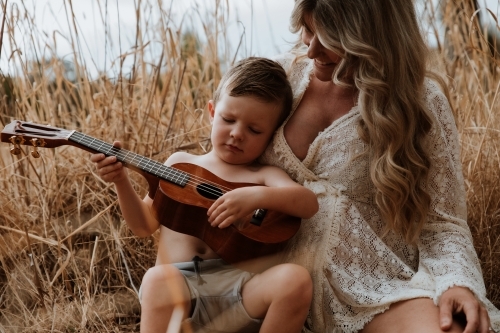 Mother and son sitting close together outside in field with small guitar - Australian Stock Image
