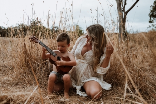 Mother and son sitting close together outside in field with small guitar - Australian Stock Image