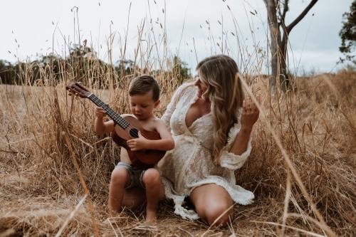 Mother and son sitting close together outside in field with small guitar