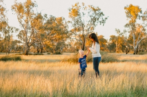 Mother and son standing in field with with long grass at sunset