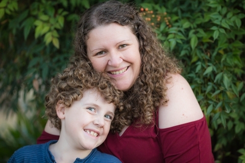 Mother and son with curly hair cuddling up in garden - Australian Stock Image