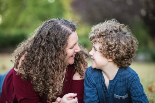 Mother and son with curly hair laying in garden looking at each other - Australian Stock Image