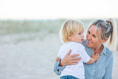 Mother and toddler son embracing on the sand of Gold Coast beach - Australian Stock Image