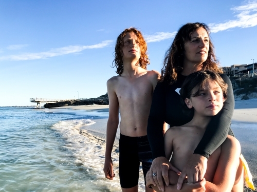 Mother and two boys playing together in ocean on calm day - Australian Stock Image