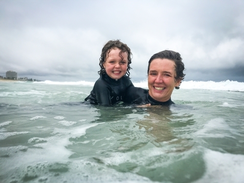 Mother and young daughter in wetsuits playing in the shores at the beach - Australian Stock Image