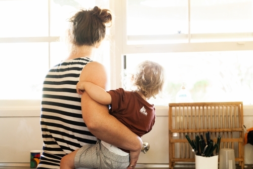 Mother at sink in the kitchen holding baby on hip