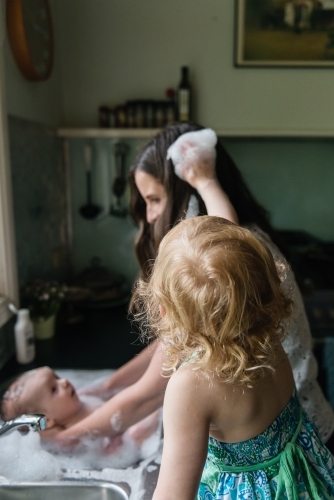 Mother bathing baby in the kitchen sink - Australian Stock Image
