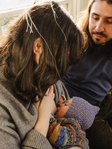 Mother breastfeeding baby wearing beanie with father sitting beside - Australian Stock Image