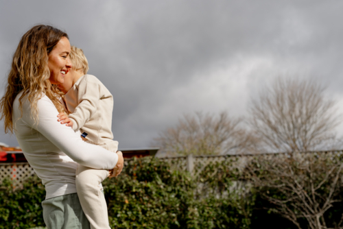 Mother carrying preschooler in a backyard with grey clouds in the background - Australian Stock Image