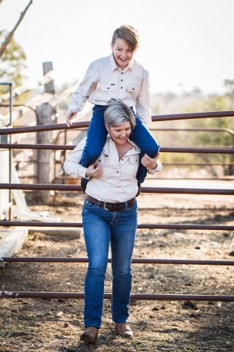 Mother carrying son on shoulders laughing on farm in drought - Australian Stock Image