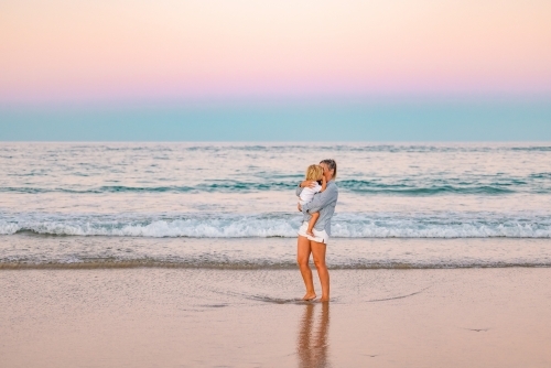 Mother carrying son on the beach in pink twilight light. Sunset on the Gold Coast. - Australian Stock Image