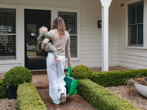 Mother carrying toddler son on one side and green shopping bag on the other - Australian Stock Image