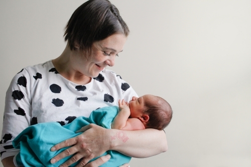 Mother cradling and smiling down at newborn baby - Australian Stock Image