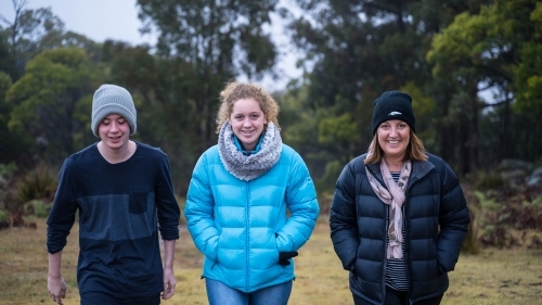 Mother, daughter and son walking on a grass field smiling - Australian Stock Image