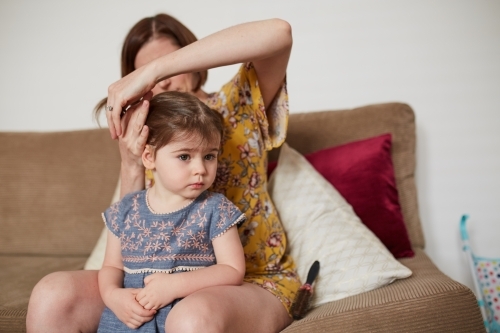 Mother doing toddler girl's hair in loungeroom - Australian Stock Image