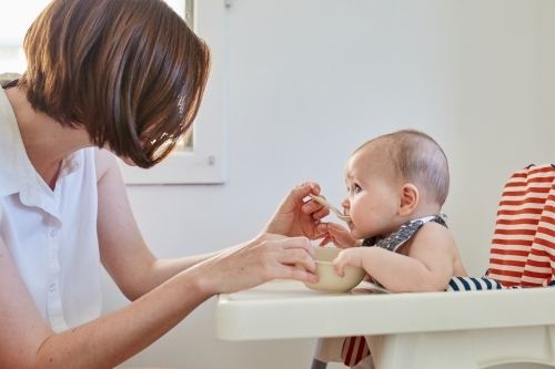 Mother feeding baby in high chair - Australian Stock Image