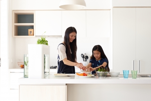 Mother helping daughter prepare a meal in kitchen - Australian Stock Image
