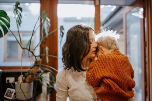 Mother holding and comforting her young son in the kitchen at home - Australian Stock Image