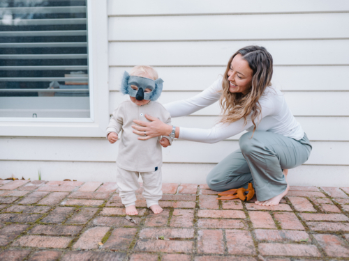 Mother holding and guiding toddler son wearing koala mask - Australian Stock Image