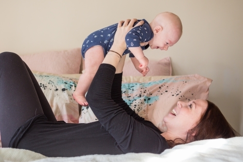 Mother holding baby son above head both smiling - Australian Stock Image