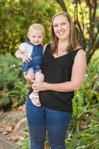 Mother holding daughter on hip smiling in garden - Australian Stock Image
