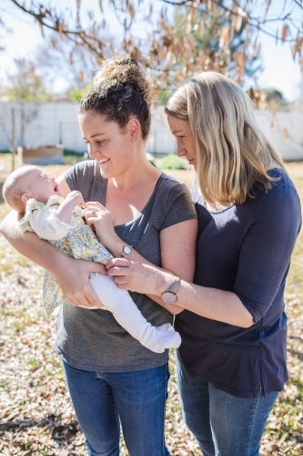 Mother holding newborn baby girl with grandmother looking and smiling - Australian Stock Image