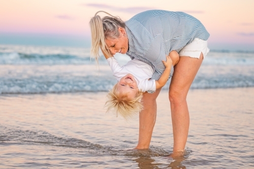 Mother holding toddler son upside down on Gold Coast beach - Australian Stock Image