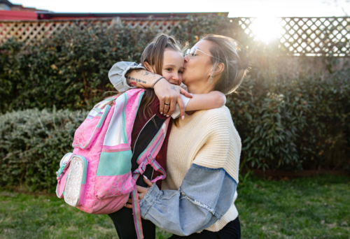 Mother hugging daughter with backpack in the garden - Australian Stock Image