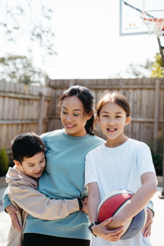 Mother hugs her two young children outside in their backyard. - Australian Stock Image