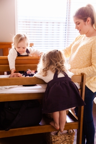 Mother in baby's room getting baby dressed sisters helping - Australian Stock Image
